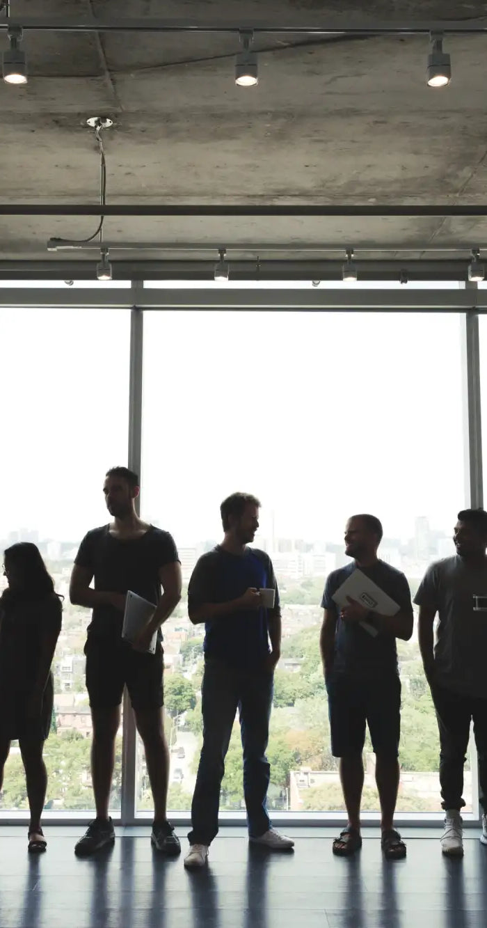 Silhouetted group of people standing in a line against large windows